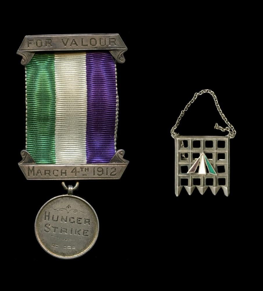 Hunger strike medal and portcullis brooch, both featuring the movement's colours of green, white and purple. The hinger strike medal bears the words 'FOR VALOUR' and the date 'MARCH 4th 1912'